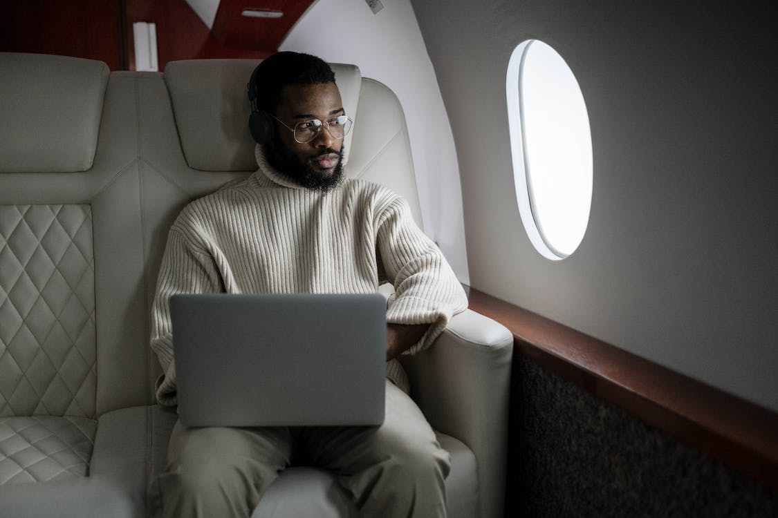 A Corporate Executive in a Turtleneck and Slacks Looking Out of the Window of their Private Jet While Using a Laptop Computer